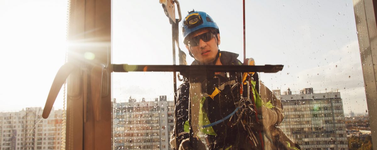 Industrial mountaineering worker hangs over residential building while washing exterior facade glazing