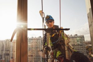 Industrial mountaineering worker hangs over residential building while washing exterior facade glazing