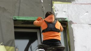 Worker man insulates wall high-rise building