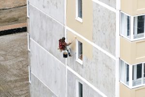 Industrial rope access worker hanging from the building while pa